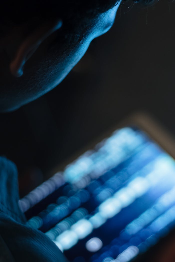 Close-up view of a person using a tablet, illuminated by its blue screen.